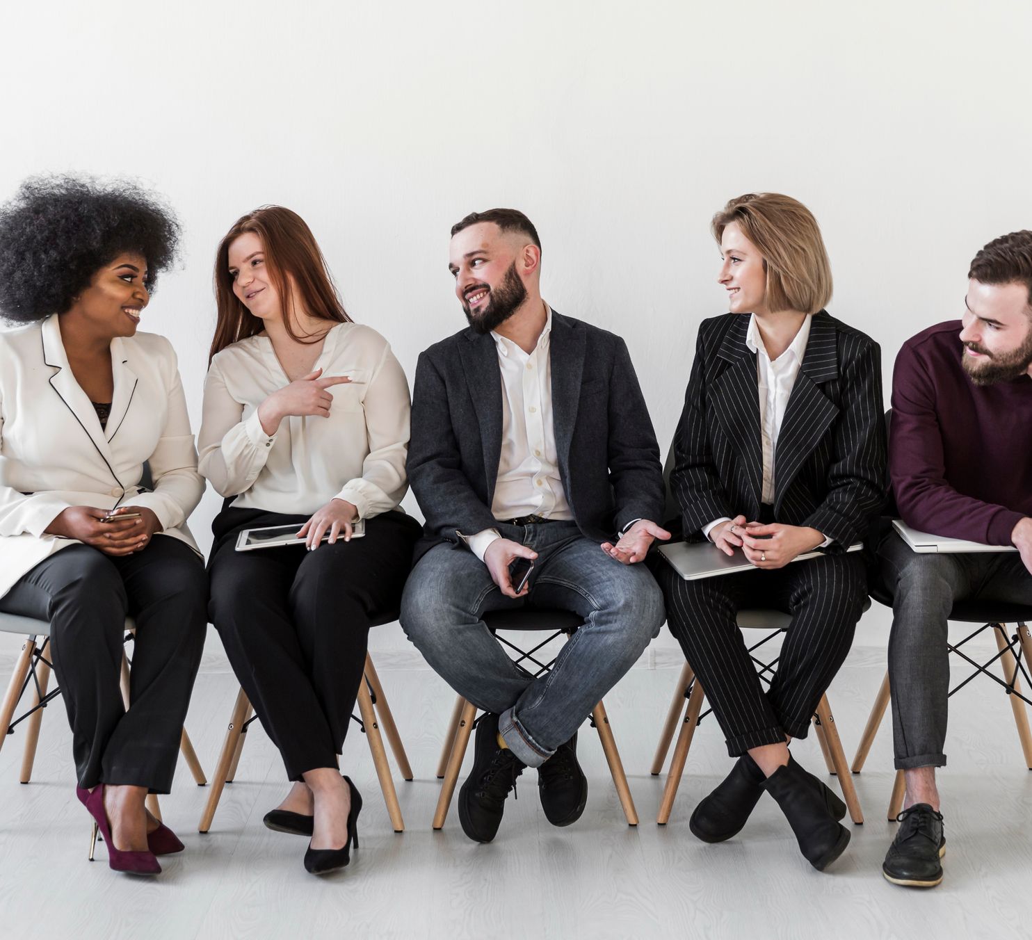 a row of people sit on a chair, with the person on the far-left mid-conversation